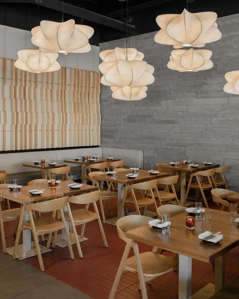 Empty modern restaurant interior, set tables and glowing fabric lights.