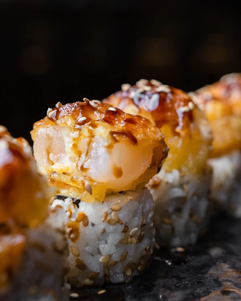 Several sushi rolls with crispy seafood, dark sauce, and sesame seeds.