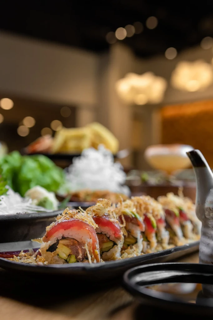 Sushi rolls topped with bonito flakes and red fish on a dark plate.