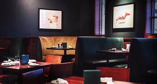 Dimly lit restaurant interior with colorful seating, set tables, and art.