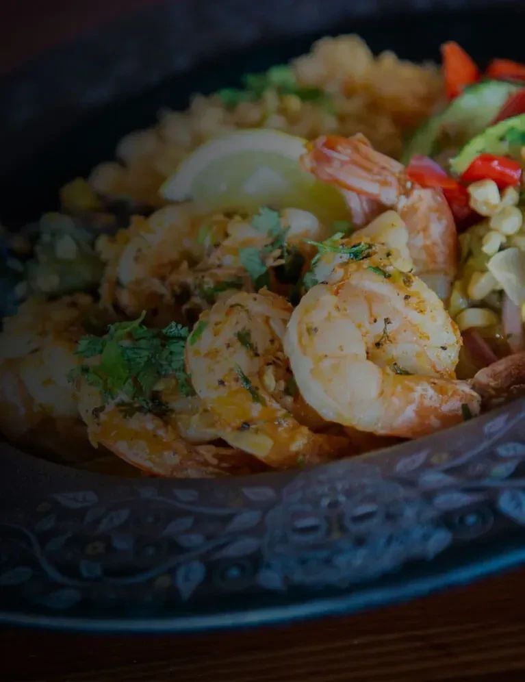 Seasoned shrimp and rice with corn, peppers, and lime in ornate bowl.