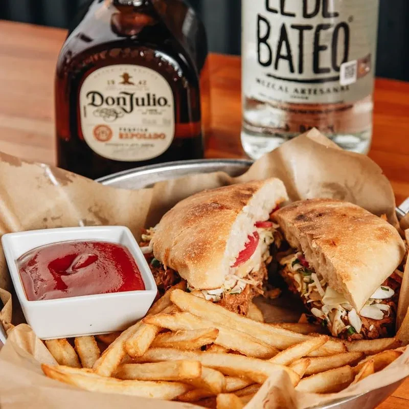 Large sandwich, fries, ketchup, and bottles of tequila and mezcal.