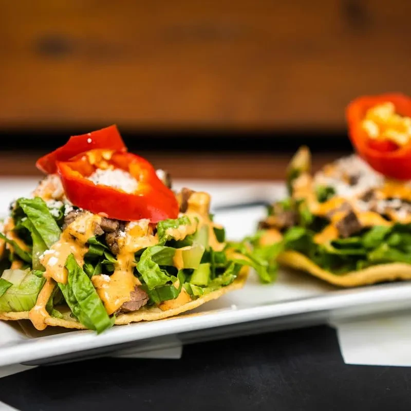 Two crispy tostadas with meat, lettuce, sauce, cheese, and red chili.