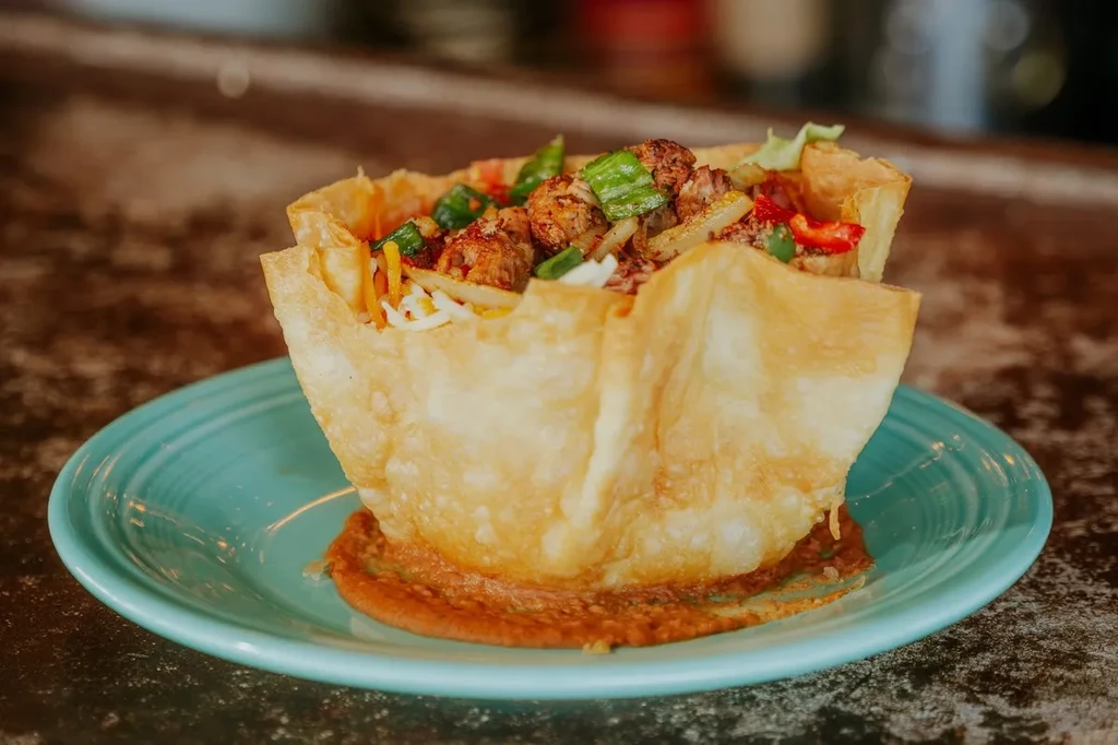 Taco salad in a fried tortilla bowl with meat, cheese, and vegetables.