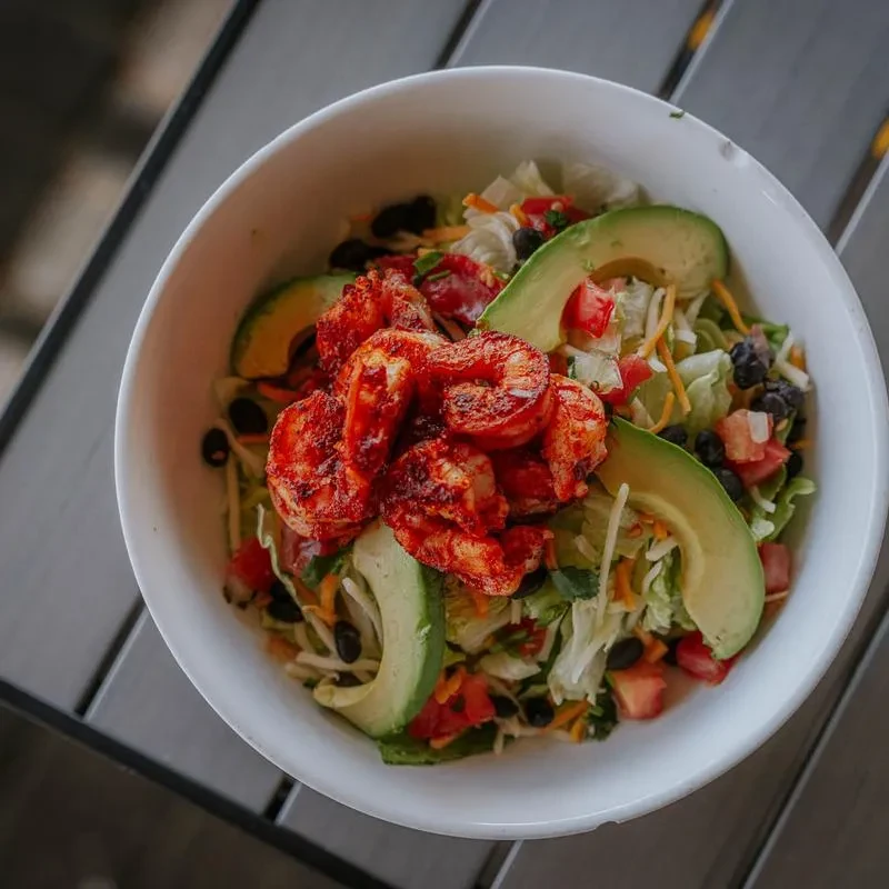 Colorful salad with seasoned shrimp, avocado, lettuce, tomatoes, and beans.