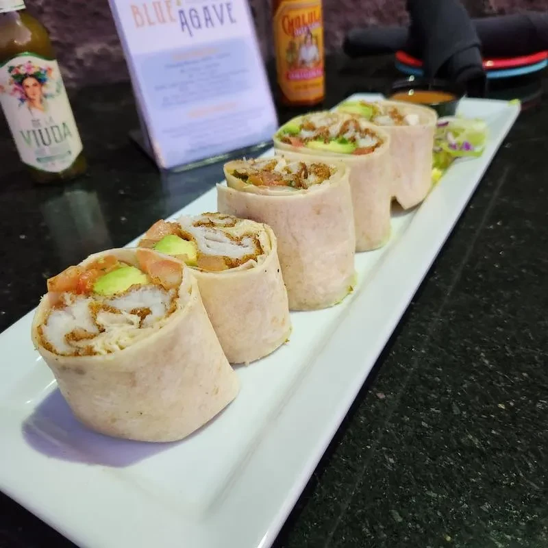 Close-up of five halved wraps with crispy fish, avocado, tomato.