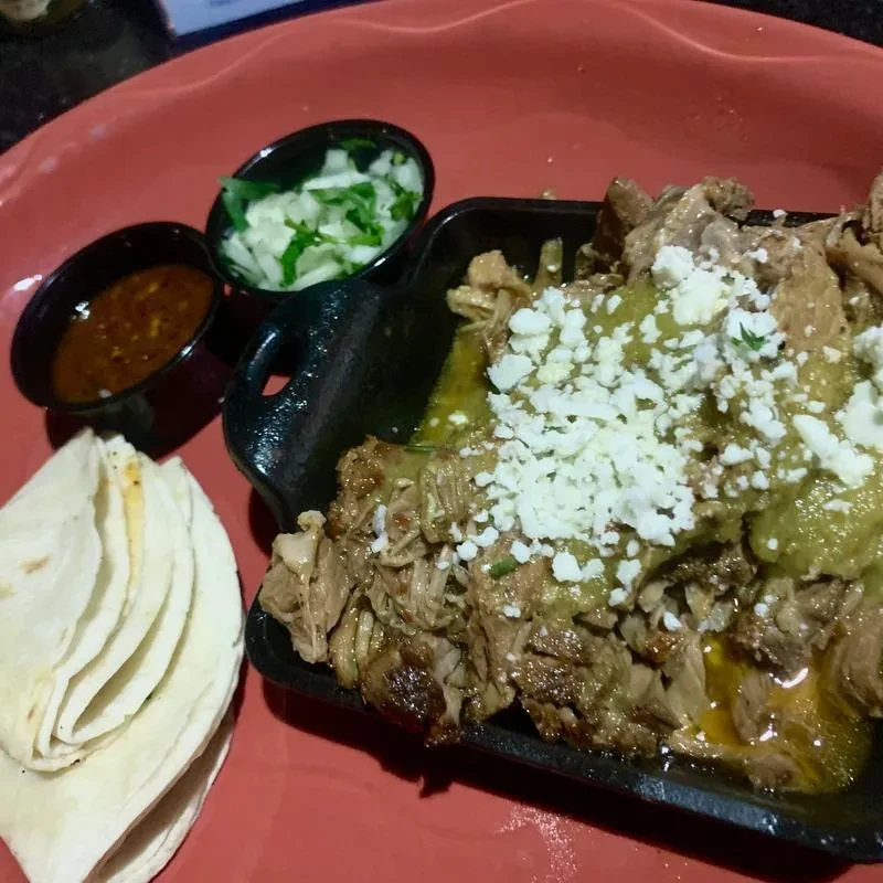 Shredded meat with green sauce, cheese, tortillas, salsa, onions, and cilantro.