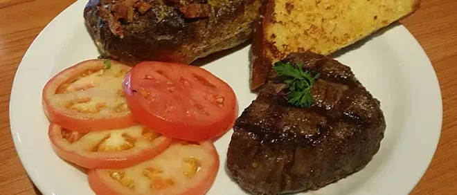 Grilled steak with baked potato, tomatoes, and garlic bread.