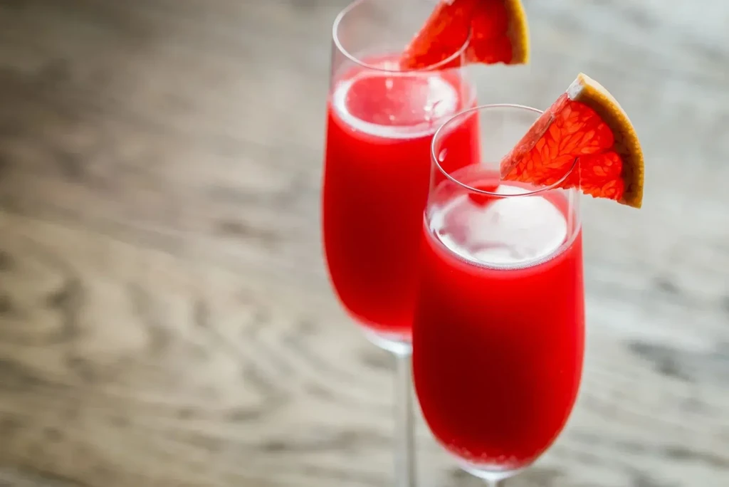 Two champagne flutes with red drinks and grapefruit wedges on wood.