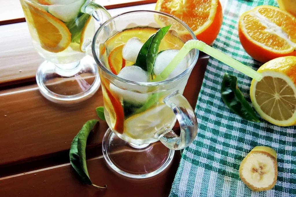 Two iced drinks with orange, lemon, and mint on a wooden table.