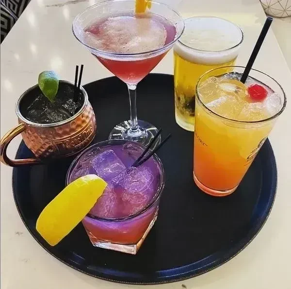 Five distinct, colorful drinks with garnishes on a black tray.