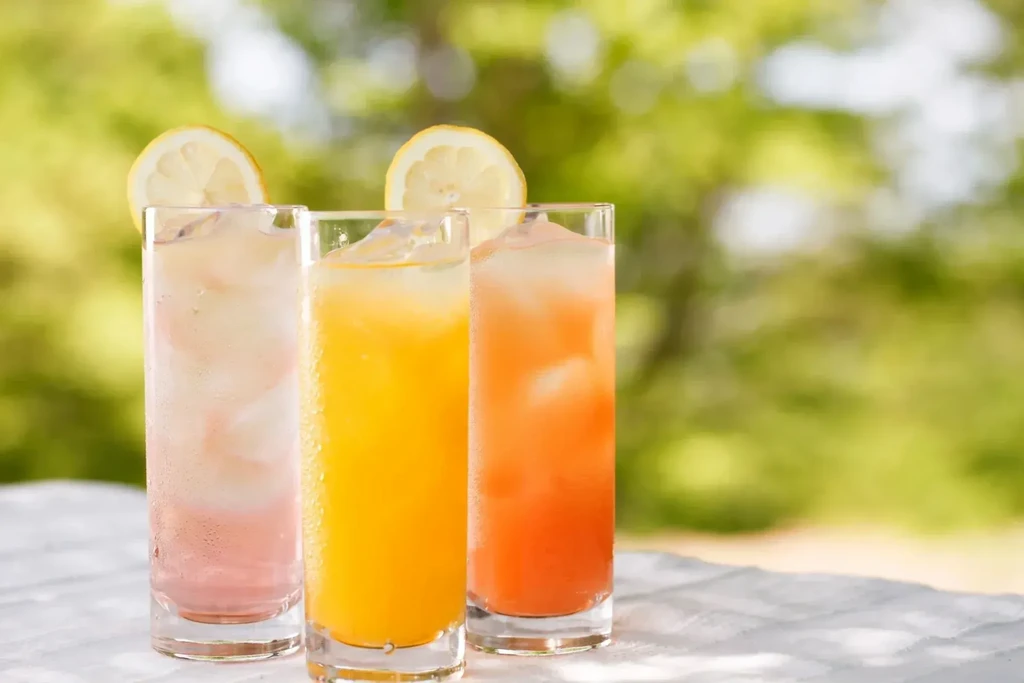 Three colorful iced drinks, lemon-garnished, in a sunny outdoor setting.