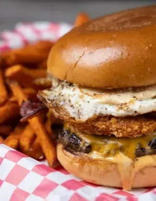 Gourmet burger with melted cheese, fried egg, bacon, and sweet potato fries.