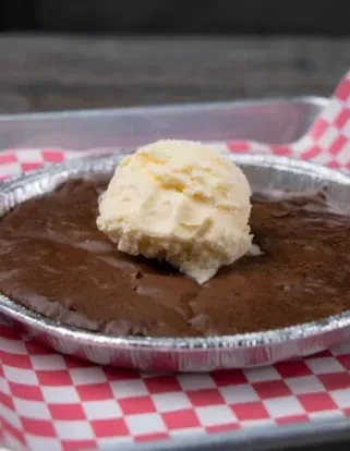 Gooey chocolate brownie with melting vanilla ice cream in a foil dish.