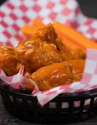 Close-up of orange, glossy chicken wings in a basket with carrots.