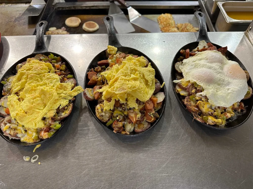 Three skillets of breakfast food with potatoes, meat, cheese, eggs.