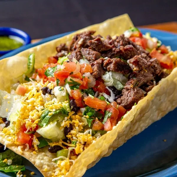 Steak taco salad in a crispy tortilla bowl on a blue plate.