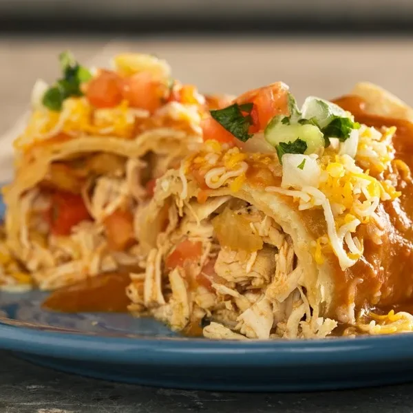 Chicken enchilada halves on blue plate, topped with sauce, cheese, and cilantro.