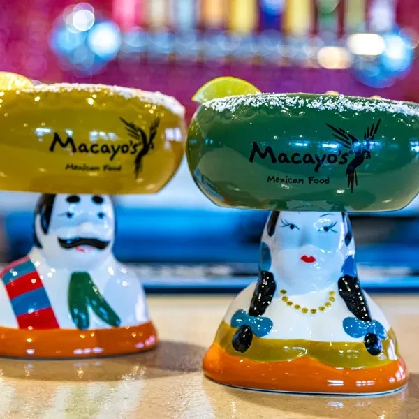 Two colorful Macayo's margaritas with unique anthropomorphic bases and lime garnishes.