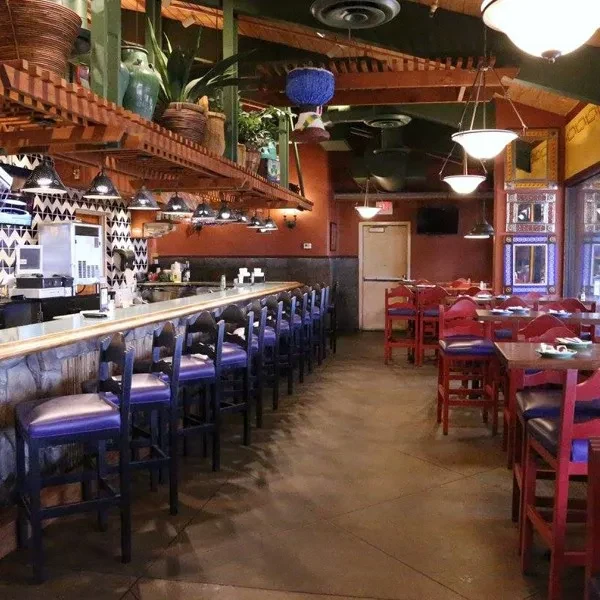 Empty restaurant bar interior with patterned wall, plants, and purple seats.