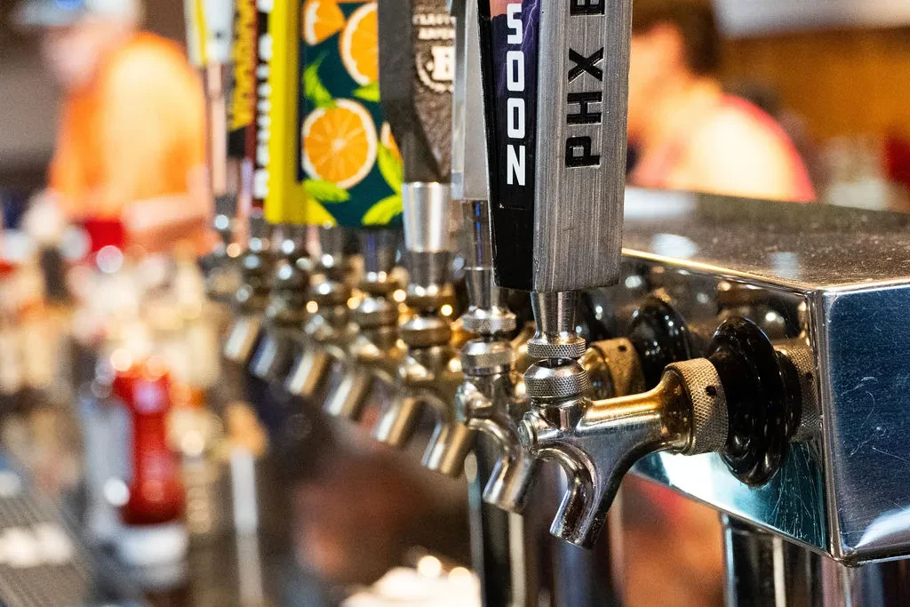 Eight diverse beer tap handles in a row, with blurred bar background.