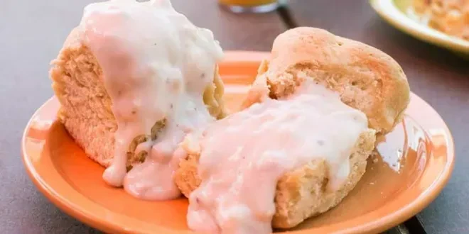Two fluffy, golden-brown biscuits with creamy gravy on an orange plate.