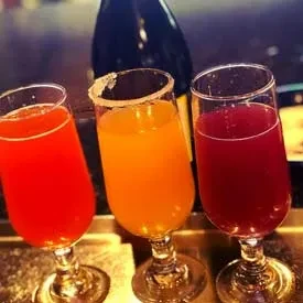 Three colorful stemmed cocktails on a bar, one sugar-rimmed.