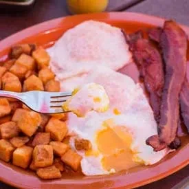 Breakfast plate with fried eggs, crispy bacon, and diced potatoes.