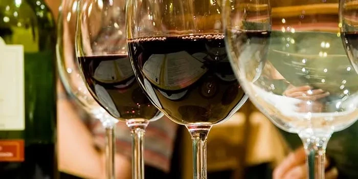 Close-up of wine glasses, most with red wine, one with clear liquid.