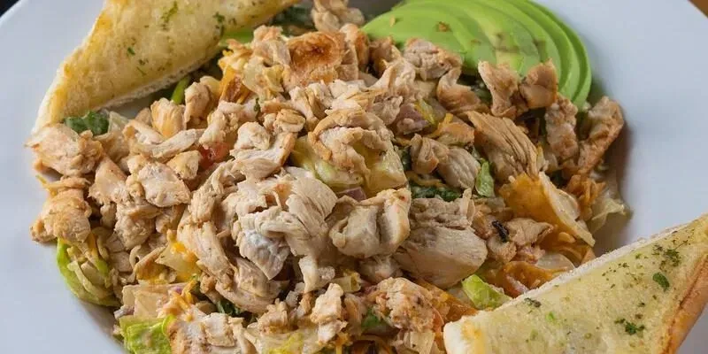 Close-up overhead view of a chicken salad with avocado and garlic bread.