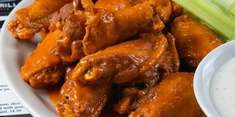 Plate of glossy orange buffalo wings, celery, and creamy dip.