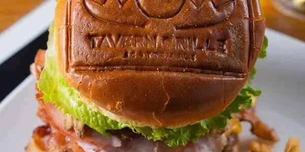 Burger with lettuce, bacon, and a bun embossed "TAVERN GRILL SCOTTSDALE".
