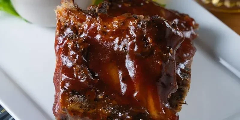 Barbecued ribs on white plate, covered in glossy red-brown sauce.