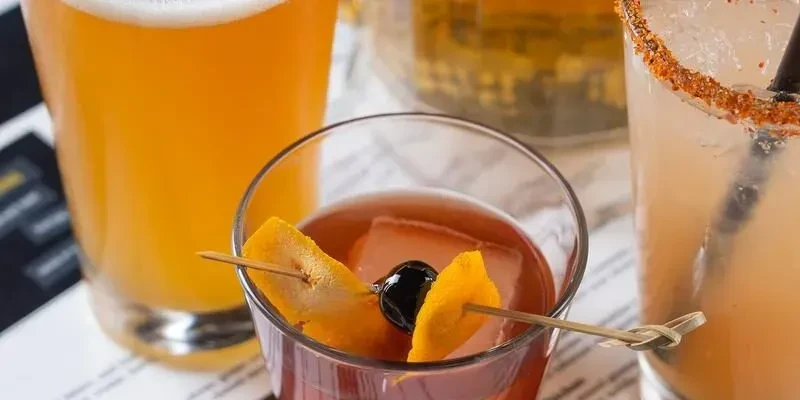 Close-up of three distinct drinks: beer, dark cocktail, rimmed cocktail.
