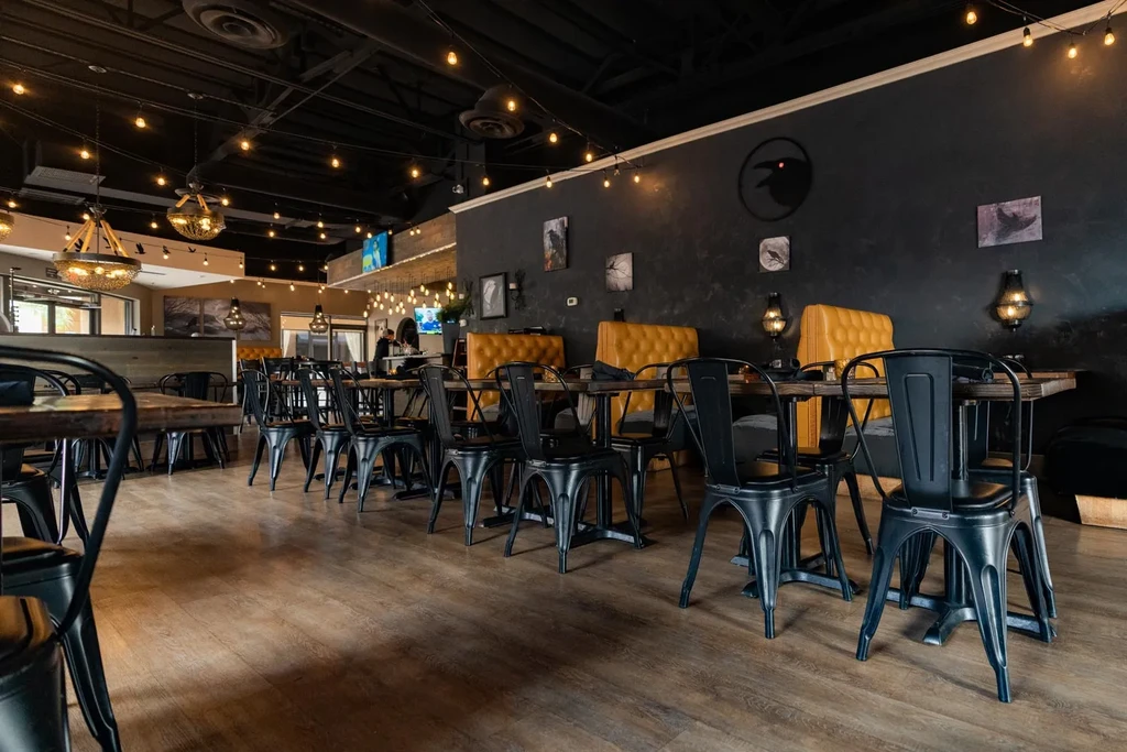 Industrial-style restaurant interior with dark tables, yellow booths, string lights.