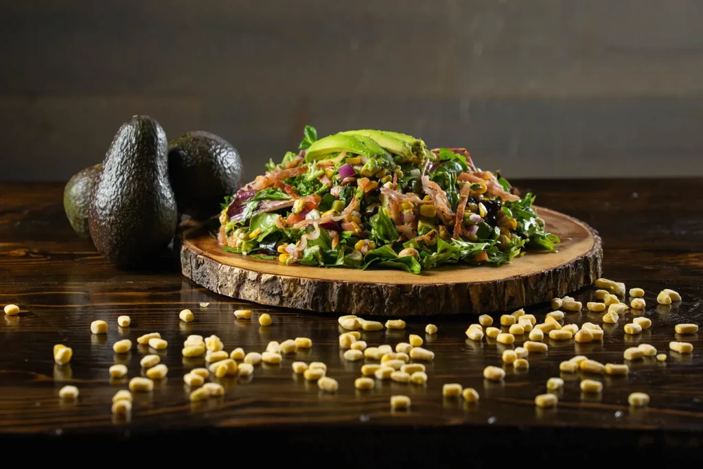 Vibrant salad with avocado, red onion, corn on a rustic wooden slab.