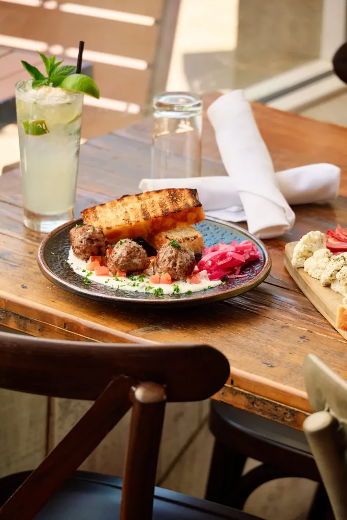 Close-up of meatballs on black plate with grilled bread and lime drink.