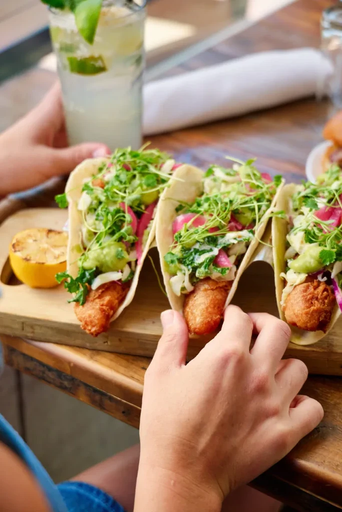 Three crispy fish tacos with microgreens and pickled onions on a board.