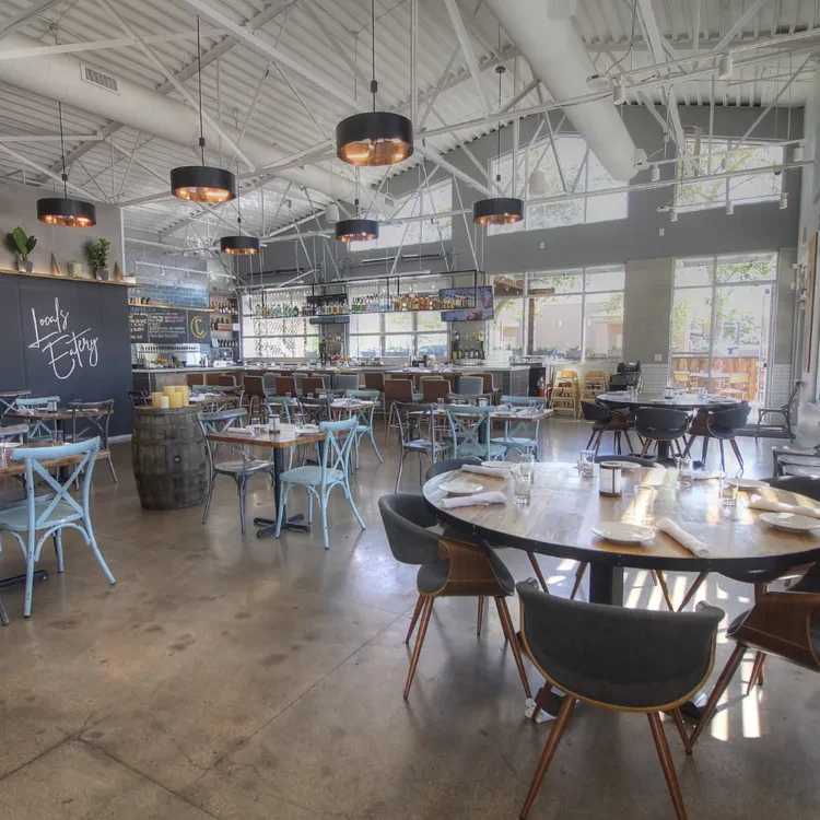 Empty modern industrial restaurant interior featuring dining tables and a prominent bar.