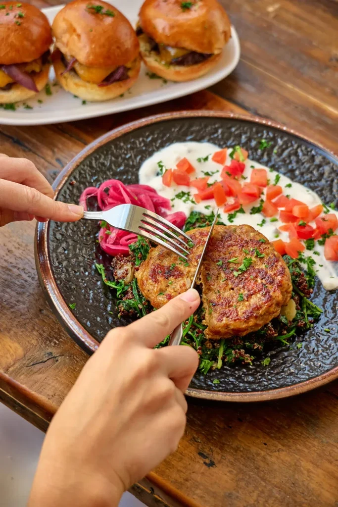 Hands cutting a meal of savory patties, quinoa, and greens.