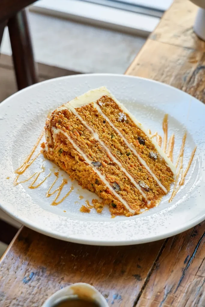 Slice of carrot cake with creamy frosting, nuts, and syrup.
