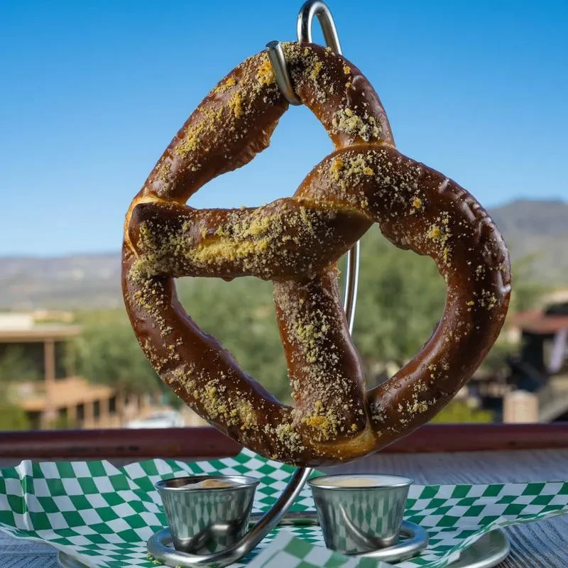 Pretzel with yellow topping, on a stand with two dips, outdoors.