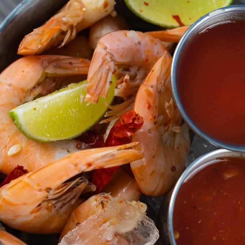 Cooked shrimp with spices, lime wedges, and two dipping sauces.