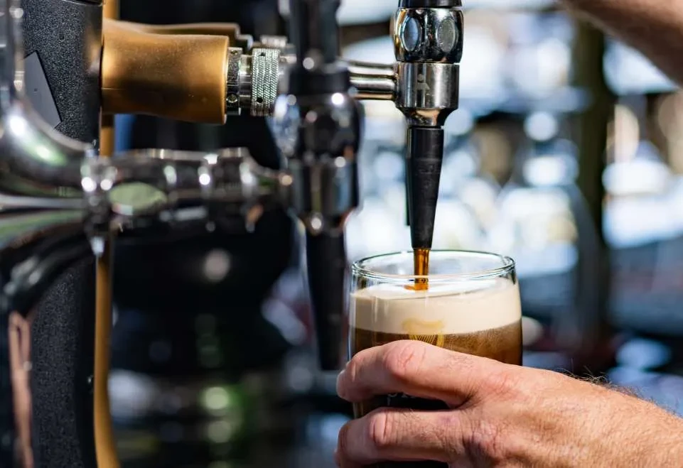 Hand holds glass filling with frothy dark beer from a tap.