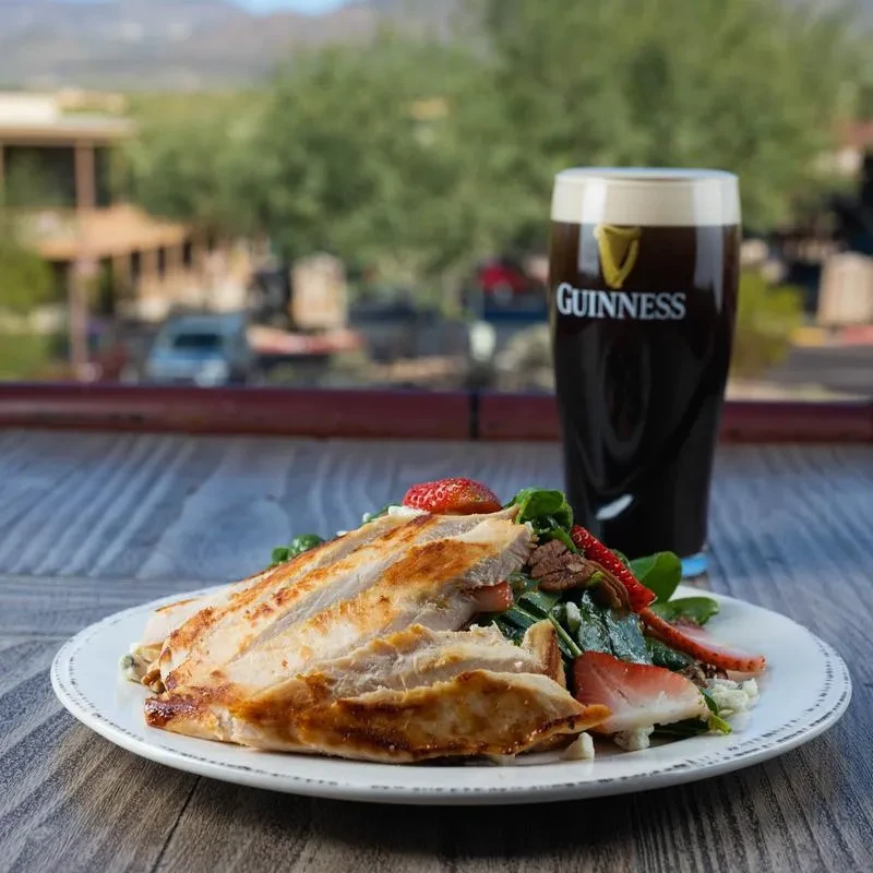 Grilled chicken salad and Guinness beer on a rustic table outdoors.
