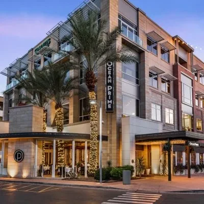 Modern building exterior with illuminated Ocean Prime restaurant and palm trees.