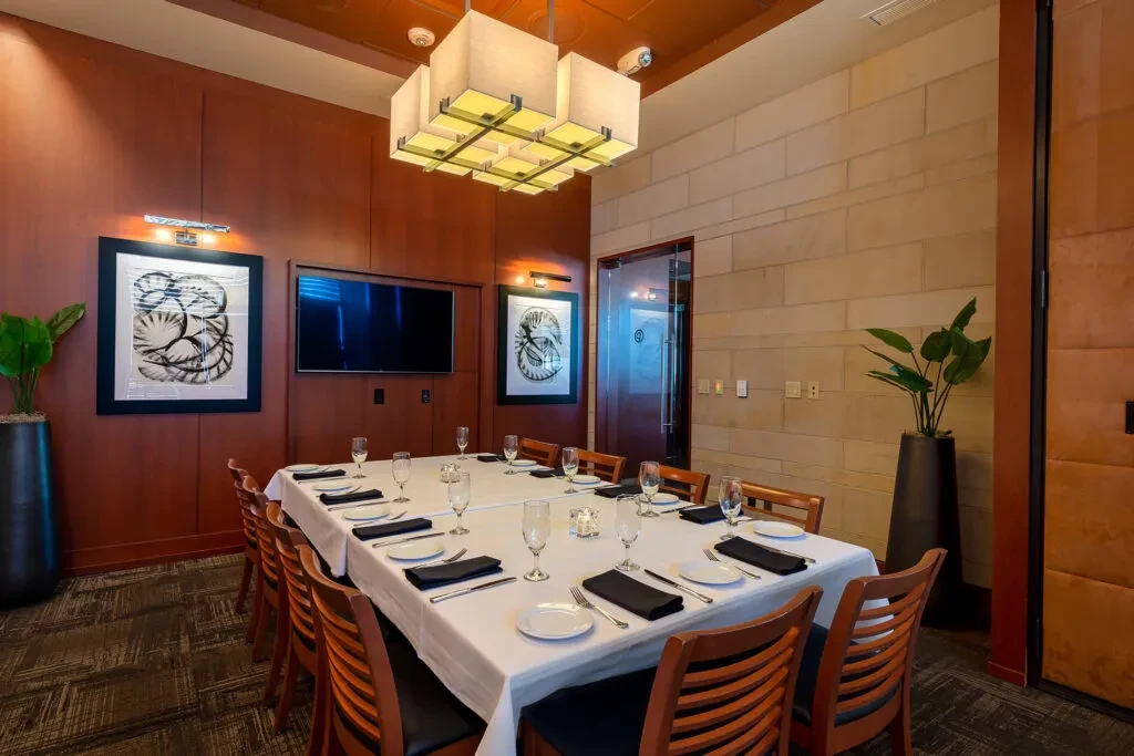 Warm private dining room, set table, wood paneling, and modern chandelier.