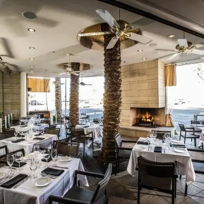 Immaculate restaurant interior with set tables, palm-like columns, lit fireplace.