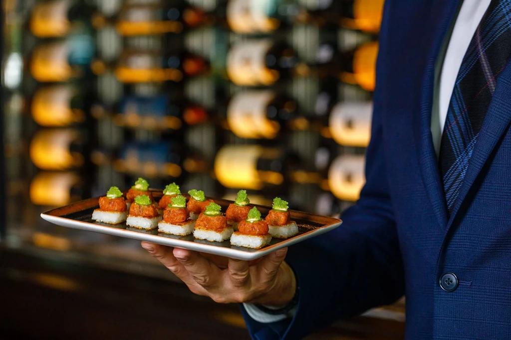 Hand holds tray of nine crispy rice pieces with tartare and green roe.