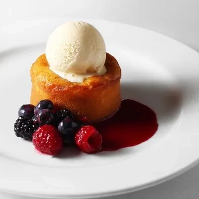 Plated cylindrical cake with vanilla ice cream, mixed berries, and red sauce.